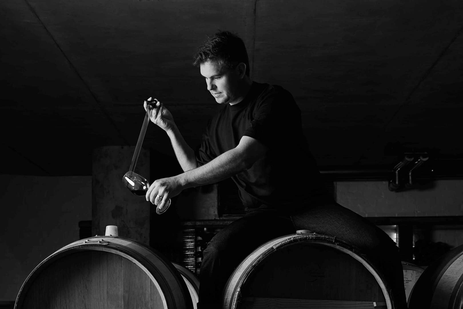 Matthew Day photographed in the Klein Constantia cellar in Cape Town by Stefan Venter Photography. Portait of wine maker sampling wine. Barrels