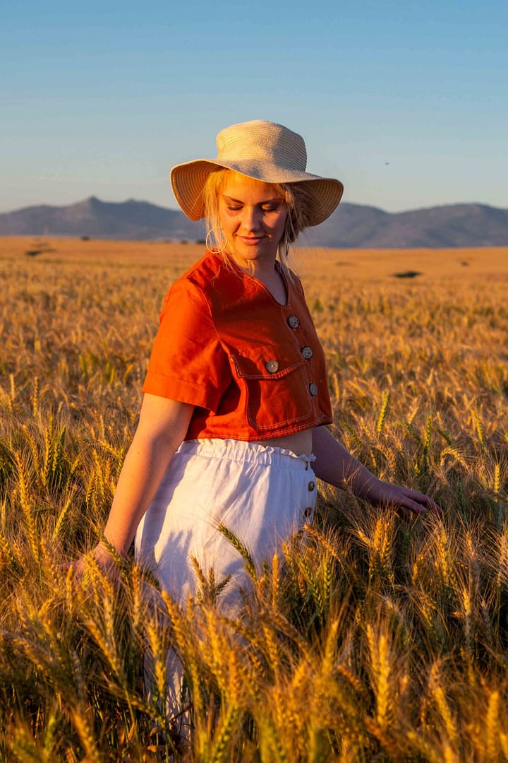 Model in a hat in a field in linen garments in Cape Town, South Africa. Photographer Stefan Venter.